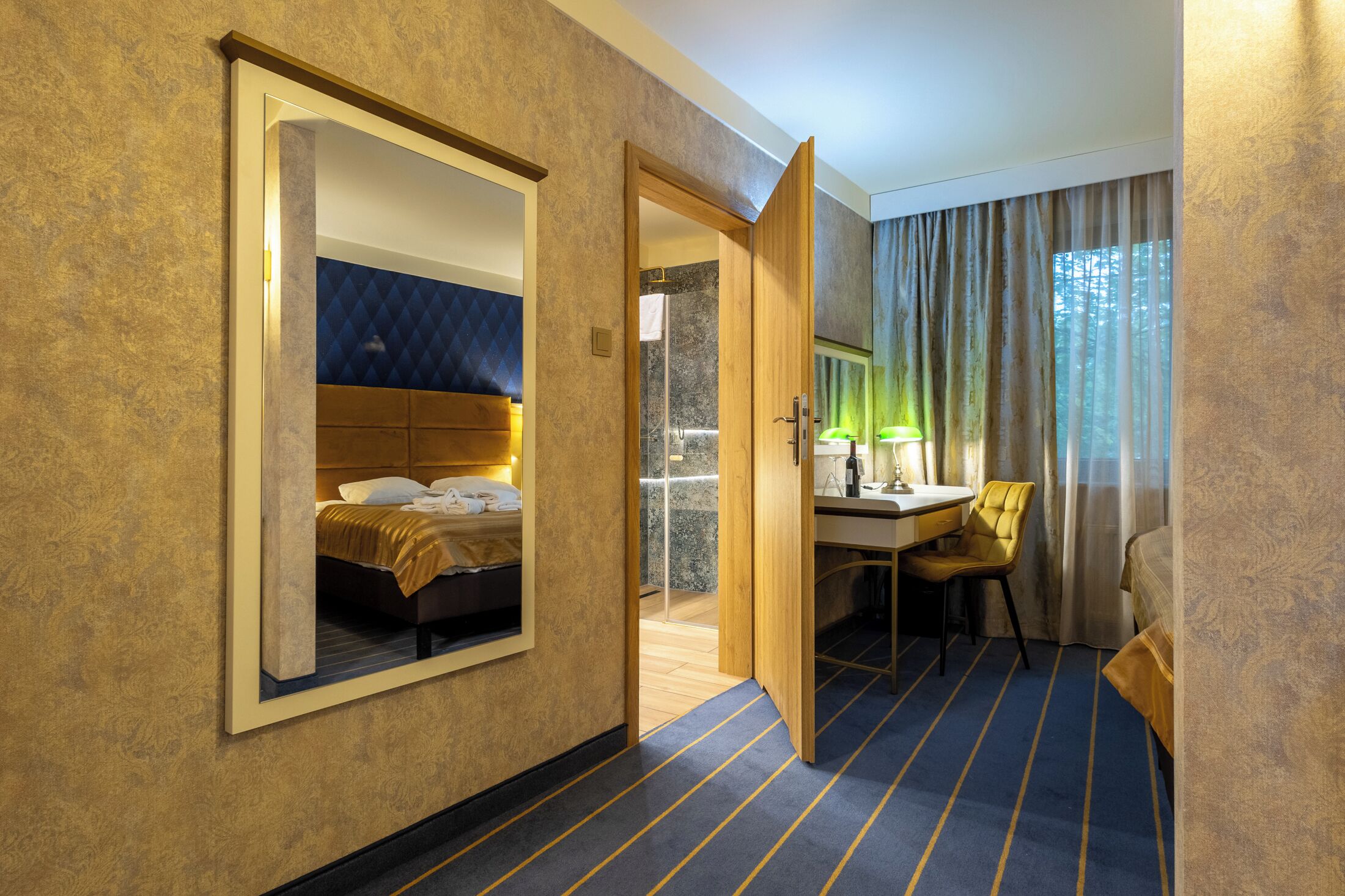 A hotel room with a bed, a desk, a chair, a mirror, a shower, and a view of the outdoors.