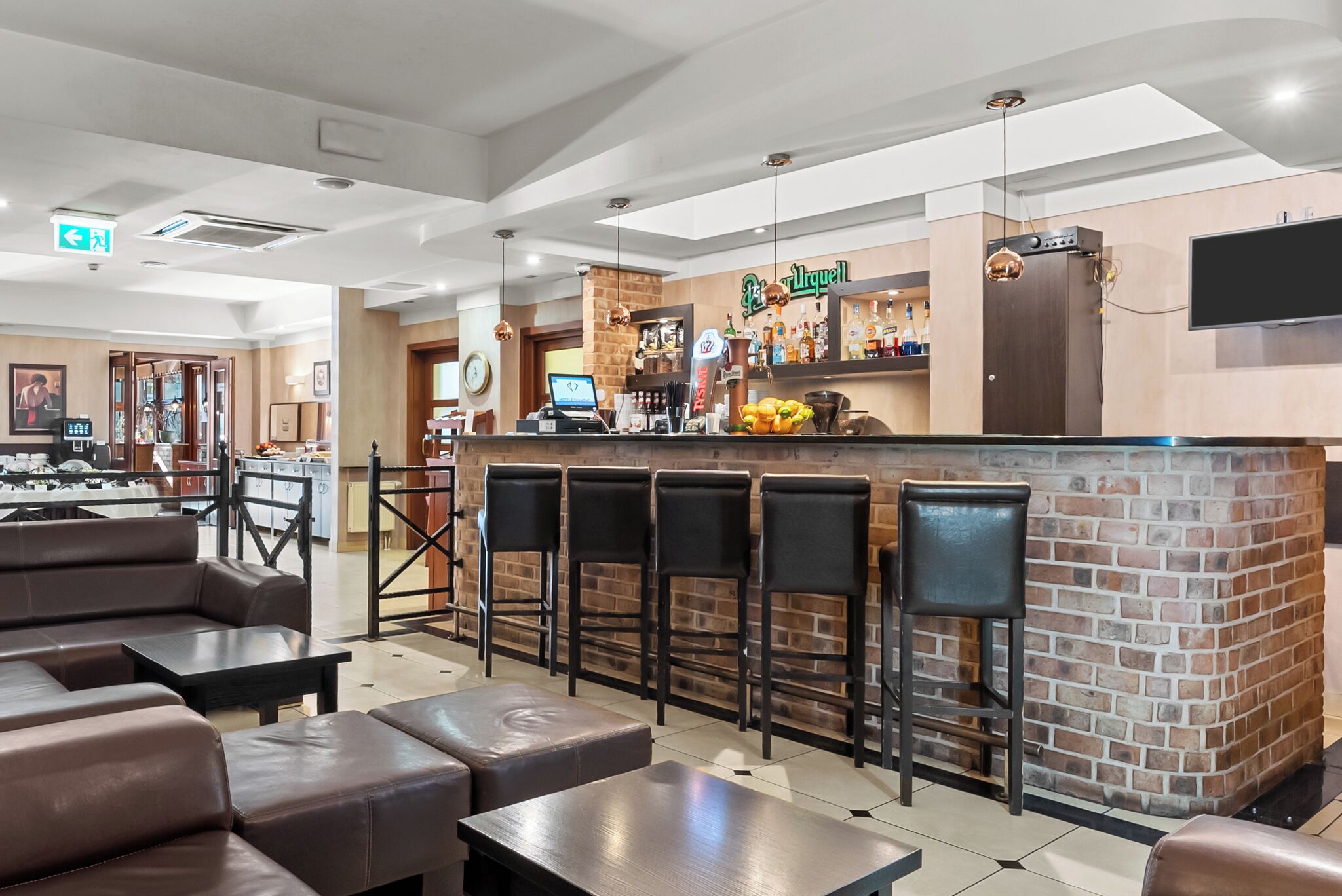 A bar area with a brick counter, multiple stools, and a seating area with tables and chairs.