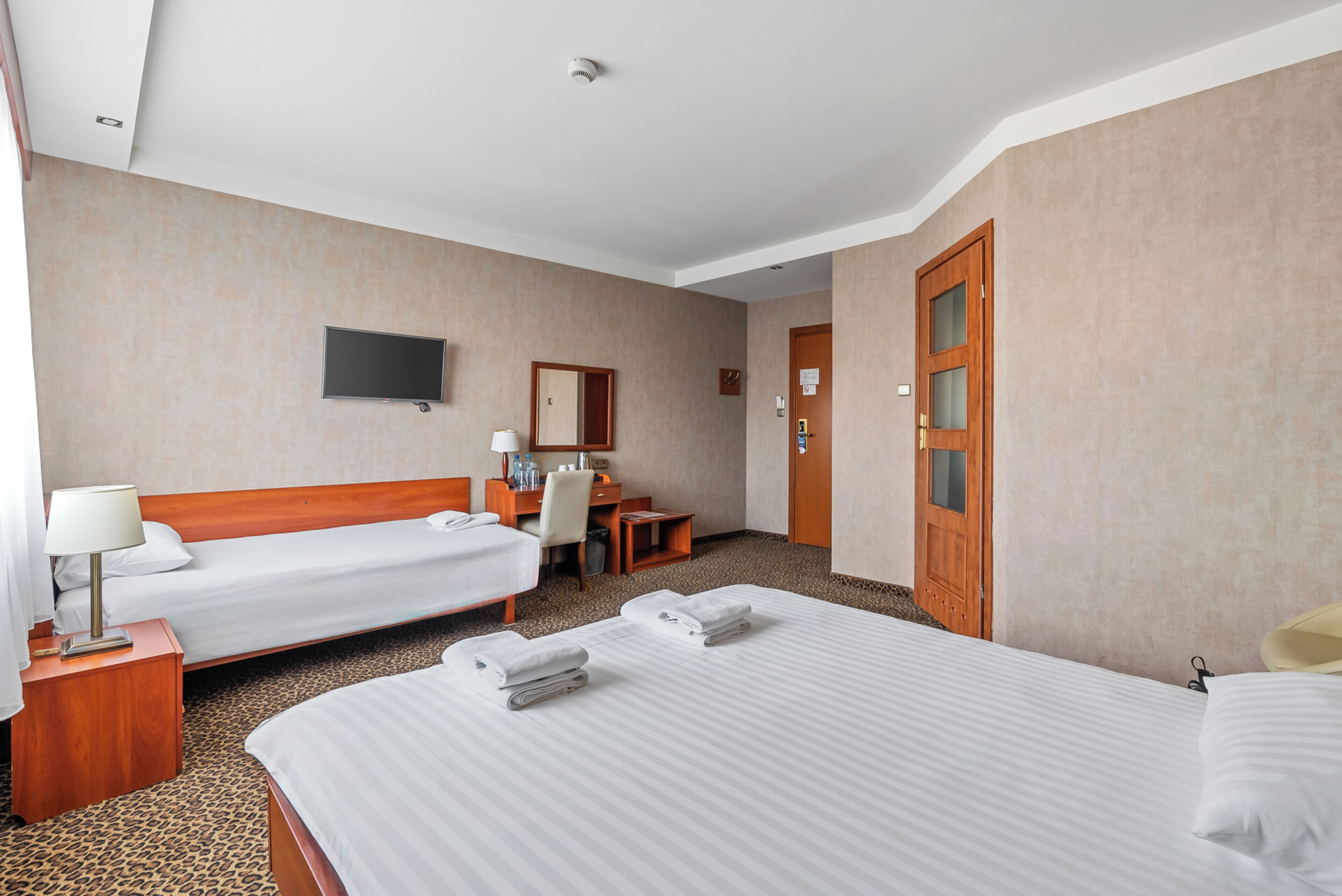 A hotel room with two beds, a desk, a chair, a flat-screen TV, and a door with a mirror.