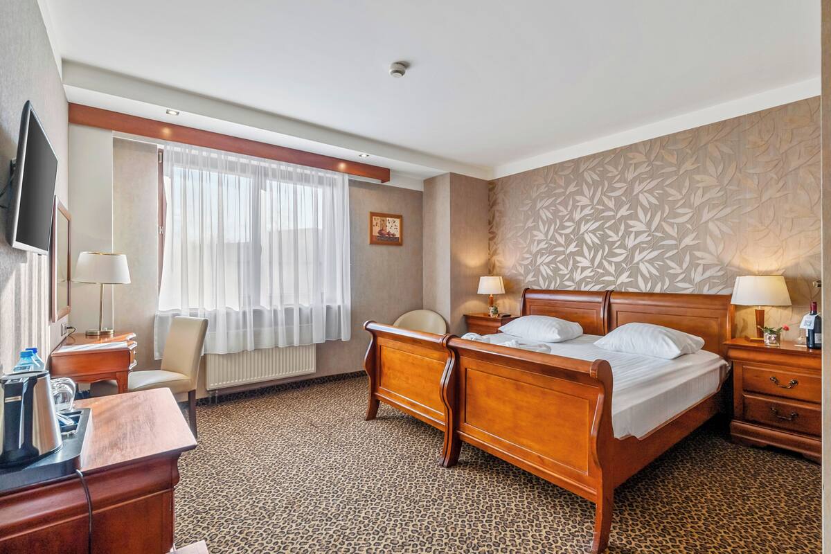 Ein Hotelzimmer mit einem Bett, Nachttischen, einem Schreibtisch mit Stuhl, einem Fernseher und einem Fenster mit Vorhängen.