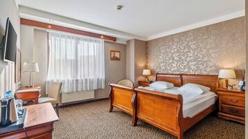 Ein Hotelzimmer mit Bett, Nachttischen, einem Schreibtisch mit Stuhl, einem Fernseher und einem Fenster mit Vorhängen.