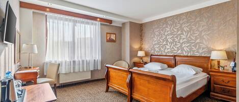 Habitación de hotel con cama, mesitas de noche, escritorio con silla, televisor y ventana con cortinas.