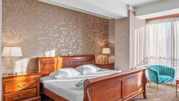Habitación de hotel con una cama de madera, dos mesitas de noche con lámparas, un papel tapiz decorativo, un sillón color turquesa y una ventana con cortinas.