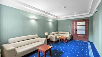 A room with a blue patterned carpet, a beige sofa, a wooden coffee table, and a wooden door with glass panels.