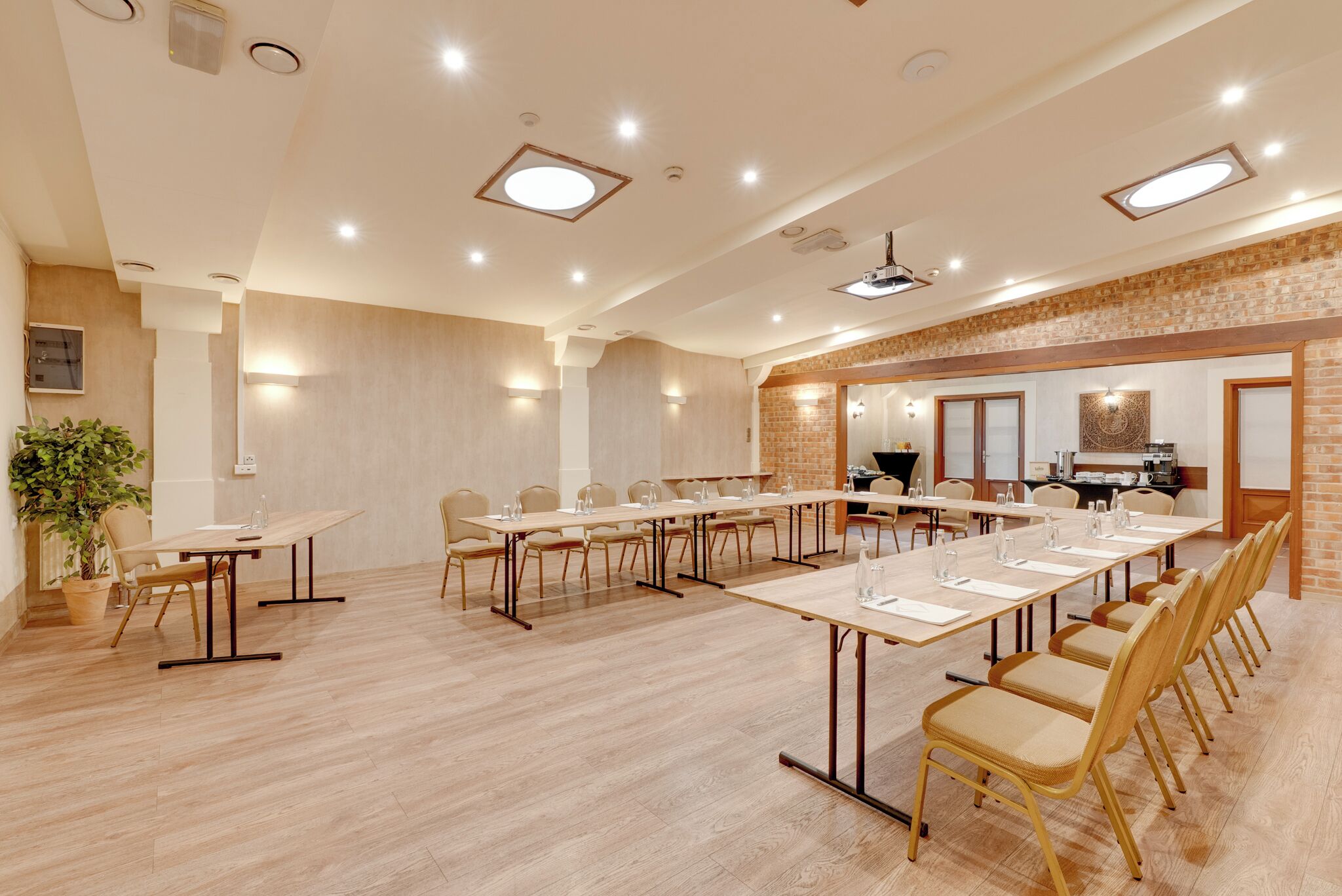 A conference room with long tables and chairs, a brick accent wall, and recessed lighting.