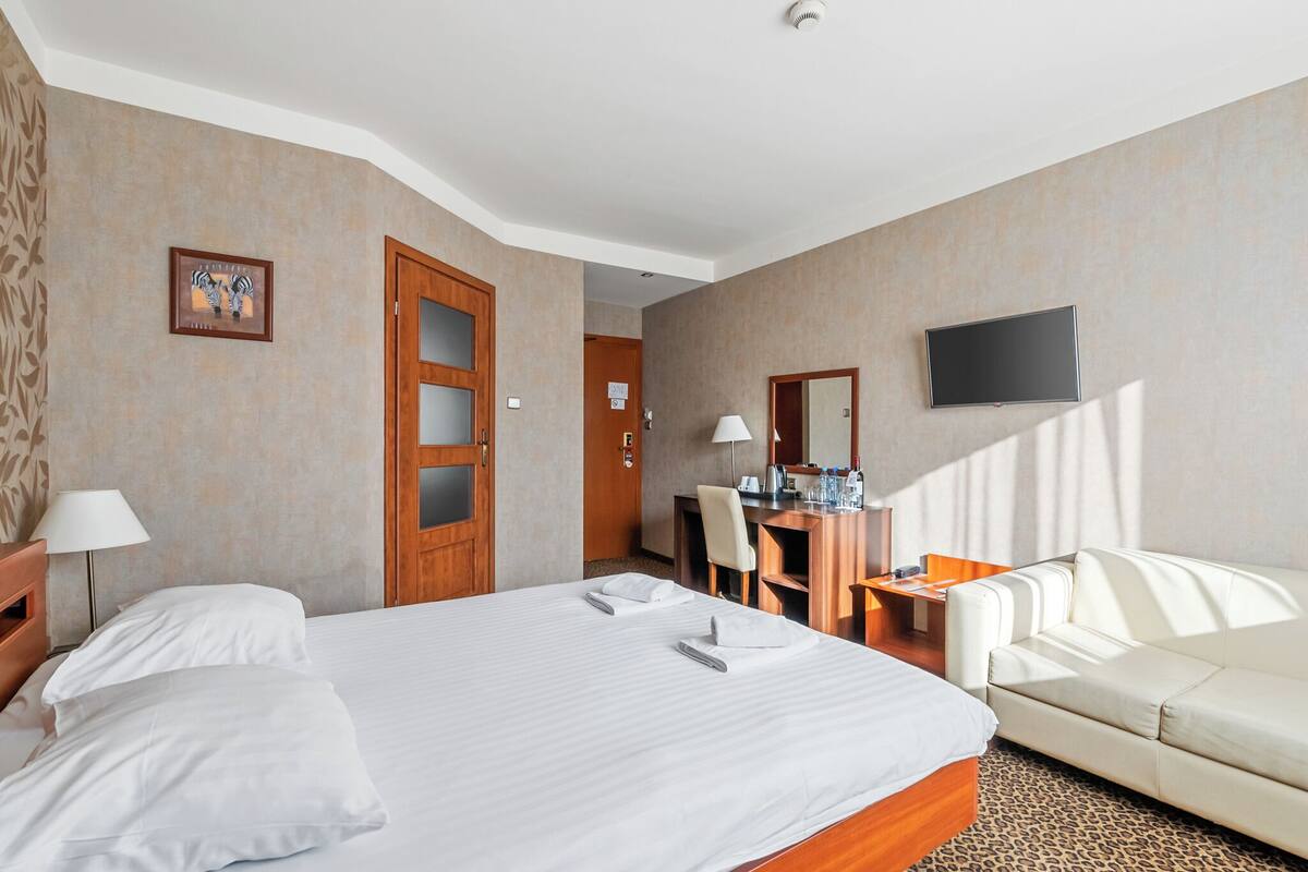 Ein Hotelzimmer mit einem großen Bett, einem Schreibtisch, einem Sessel, einem Sofa, einem Fernseher und einer Tür zu einem anderen Raum.