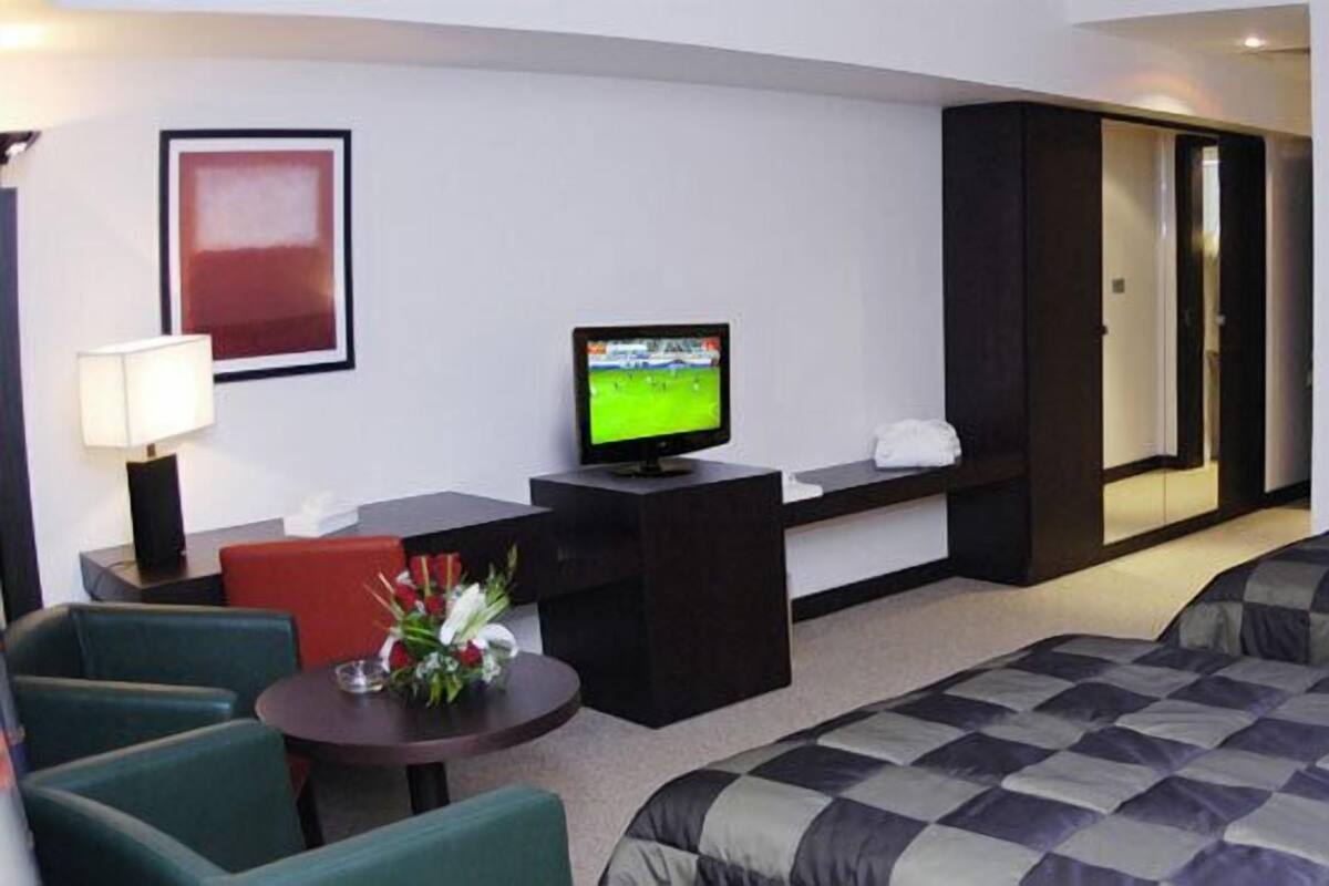 Ein Hotelzimmer mit einem Bett, einem Schreibtisch mit Fernseher, einem Sessel und einem kleinen Tisch mit Blumen.