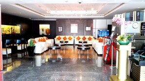 A modern hotel lobby with a reception desk, seating area with sofas and round tables, a large screen, and a clock. - Al Jazira Club Hotel (Abu Dhabi)