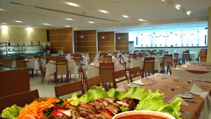 A restaurant with multiple tables and chairs, a buffet area, and a view of the city through large windows. - Al Jazira Club Hotel (Abu Dhabi)