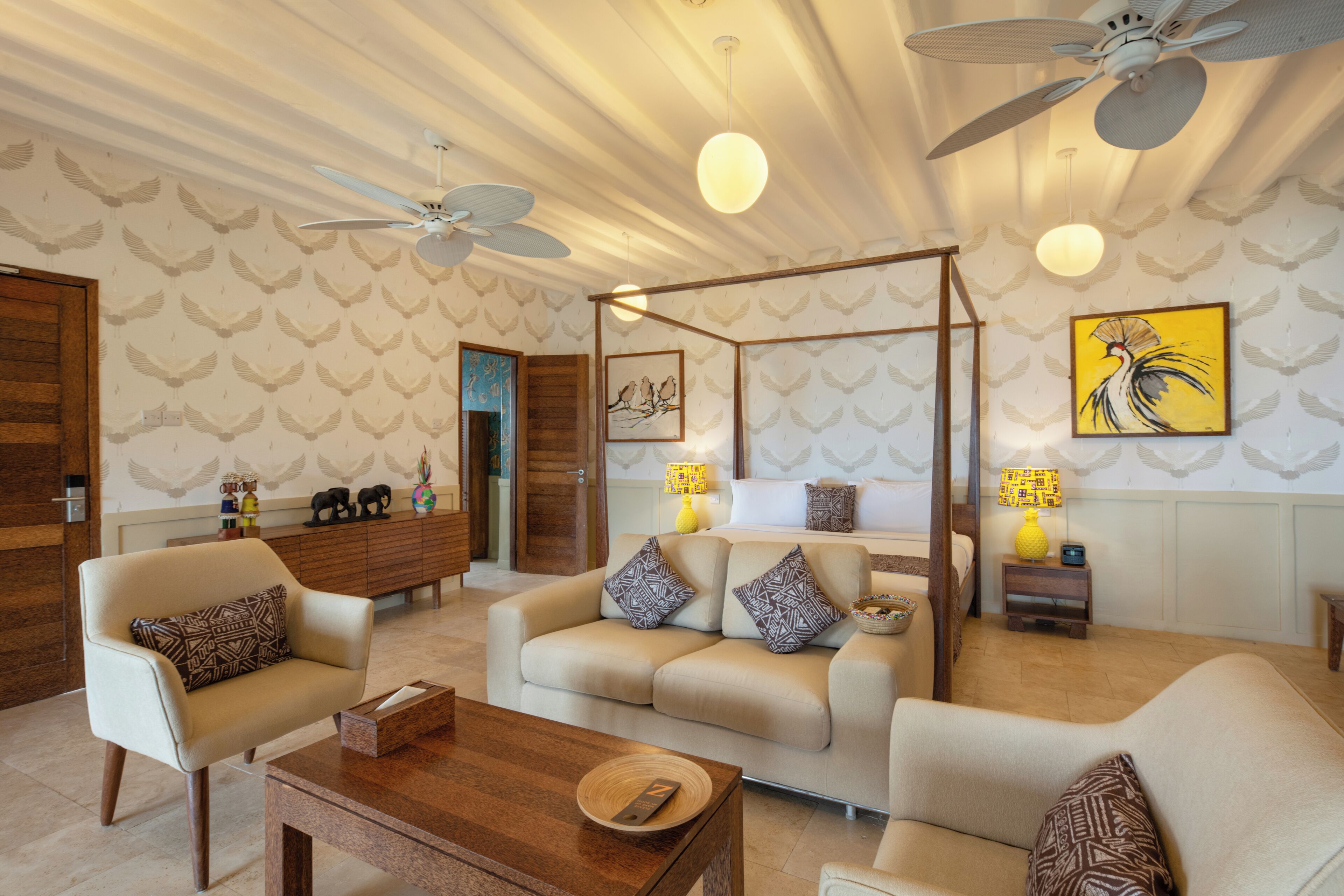 A well-lit living room with a ceiling fan, a sofa set, a coffee table, and a decorative wall with a bird pattern.