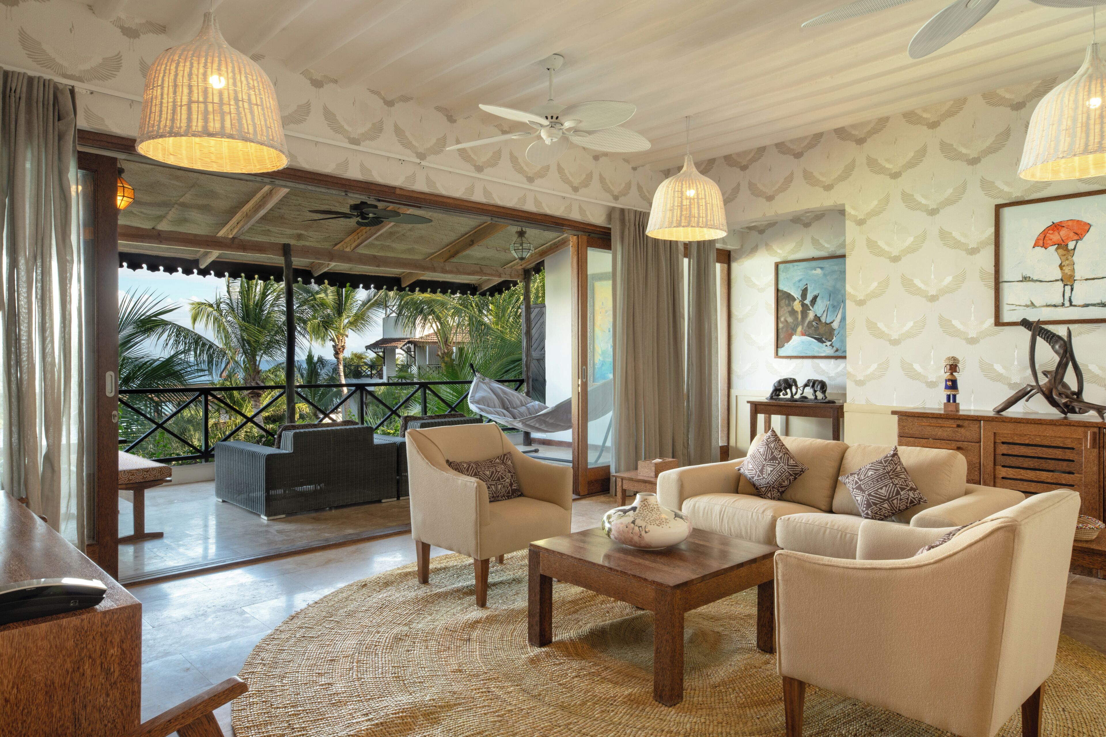 A spacious living area with a sofa set, a coffee table, and a hanging chair. There is a view of palm trees through the glass doors.
