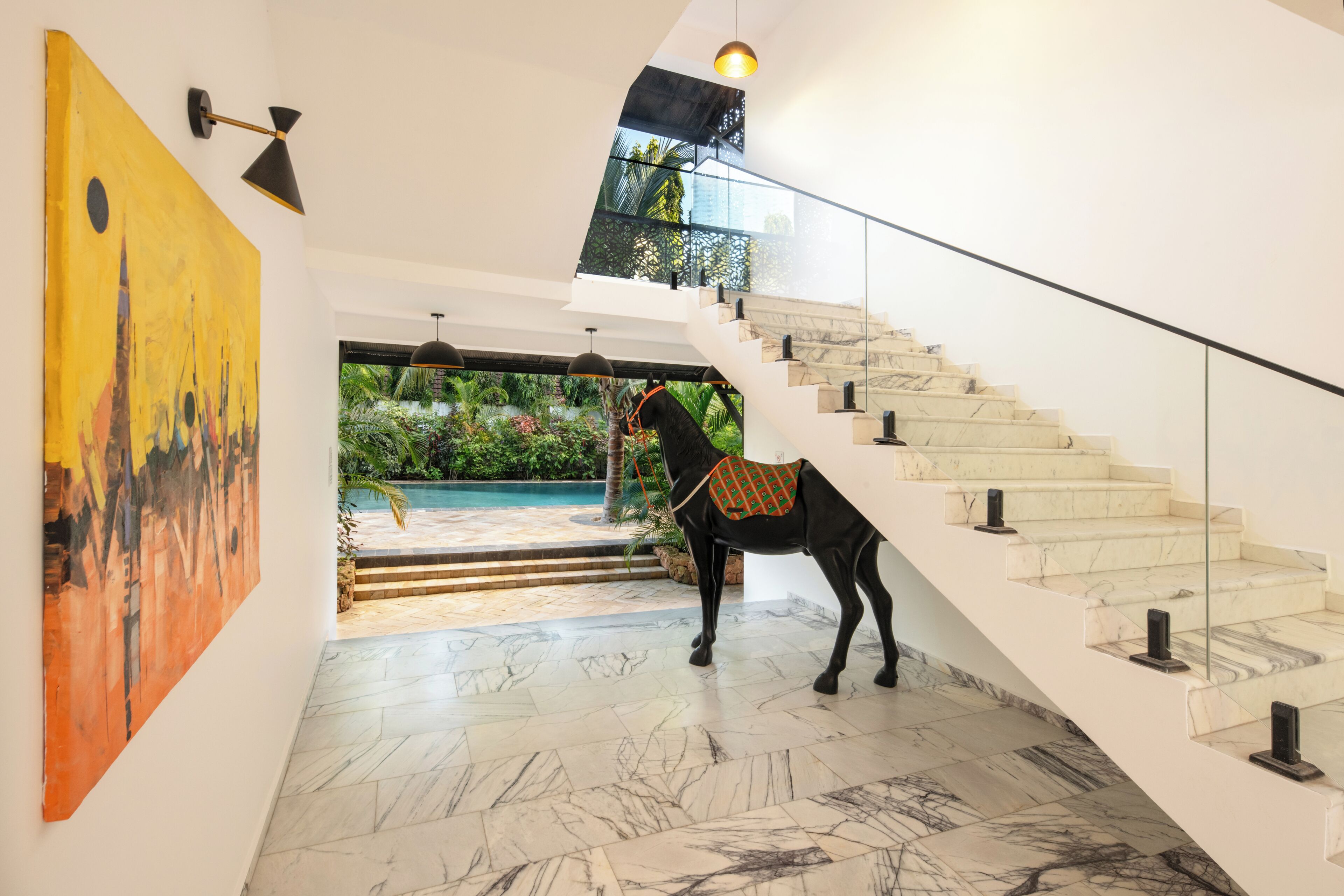 A modern interior with a staircase, a horse statue, and a pool view.