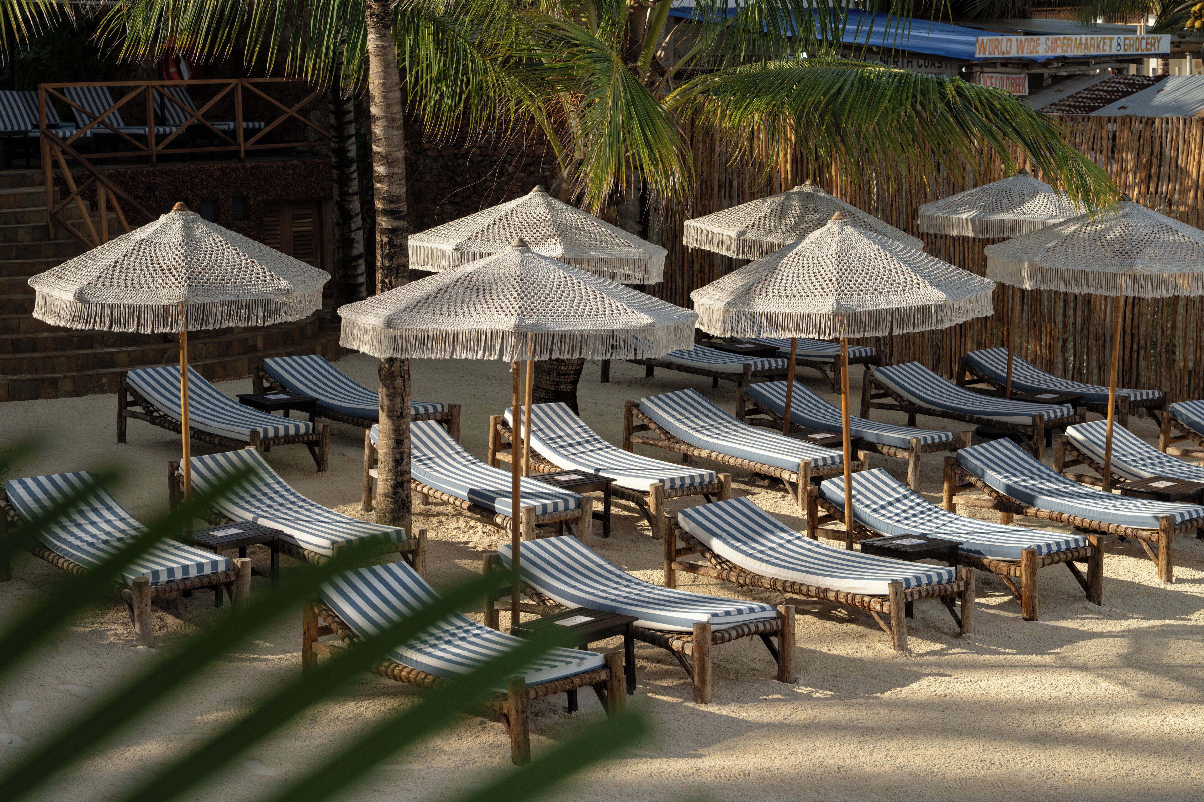 Un espace de détente aménagé sur la plage, avec des chaises longues à rayures et des parasols en osier.
