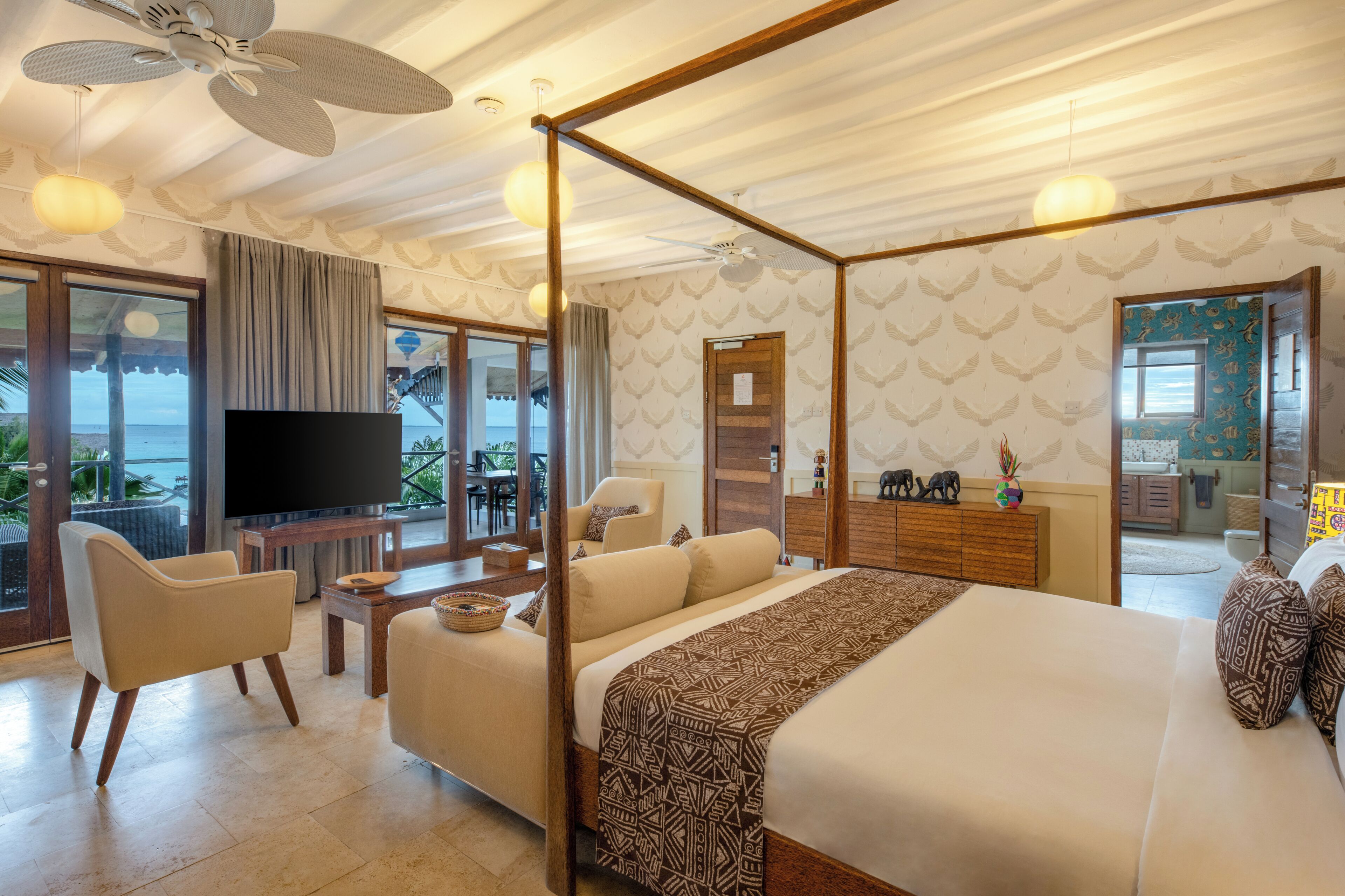 A spacious bedroom with a four-poster bed, a television, and a balcony with a view of the sea.