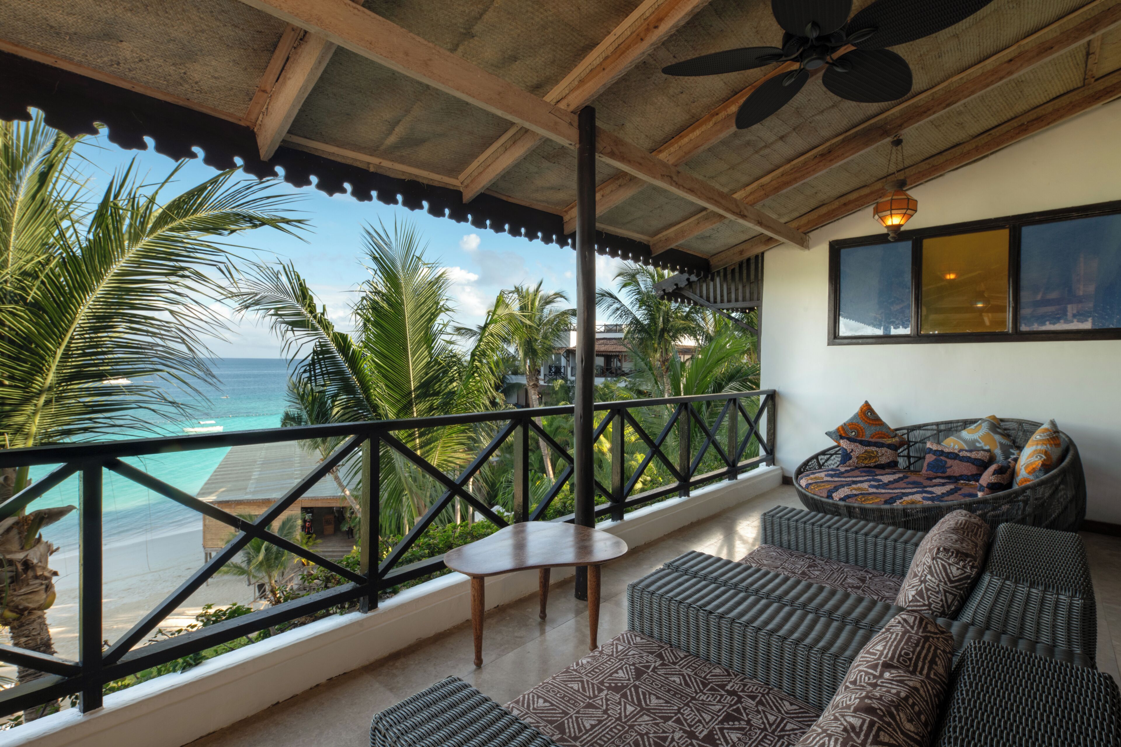 A balcony with a view of the ocean, a ceiling fan, and a wicker sofa with cushions.