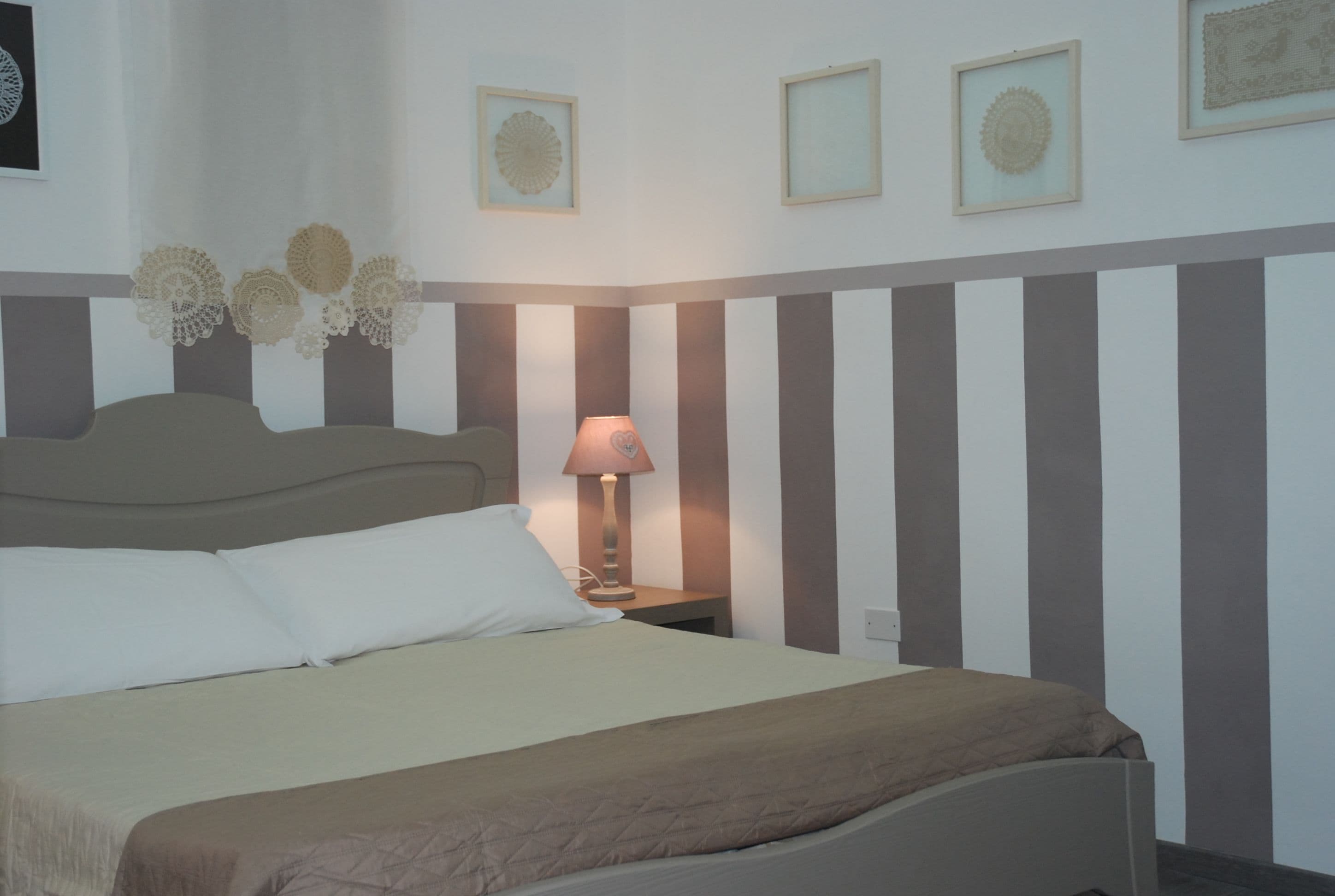 Una cama bien hecha con ropa de cama blanca y marrón, una lámpara de noche y decoración en la pared.