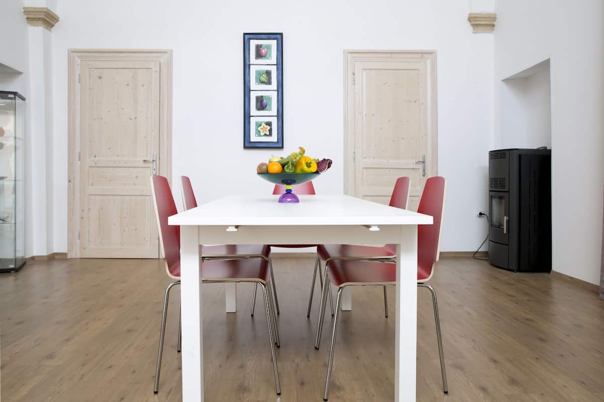 A dining area with a white table, red chairs, a fruit bowl, and a black appliance.