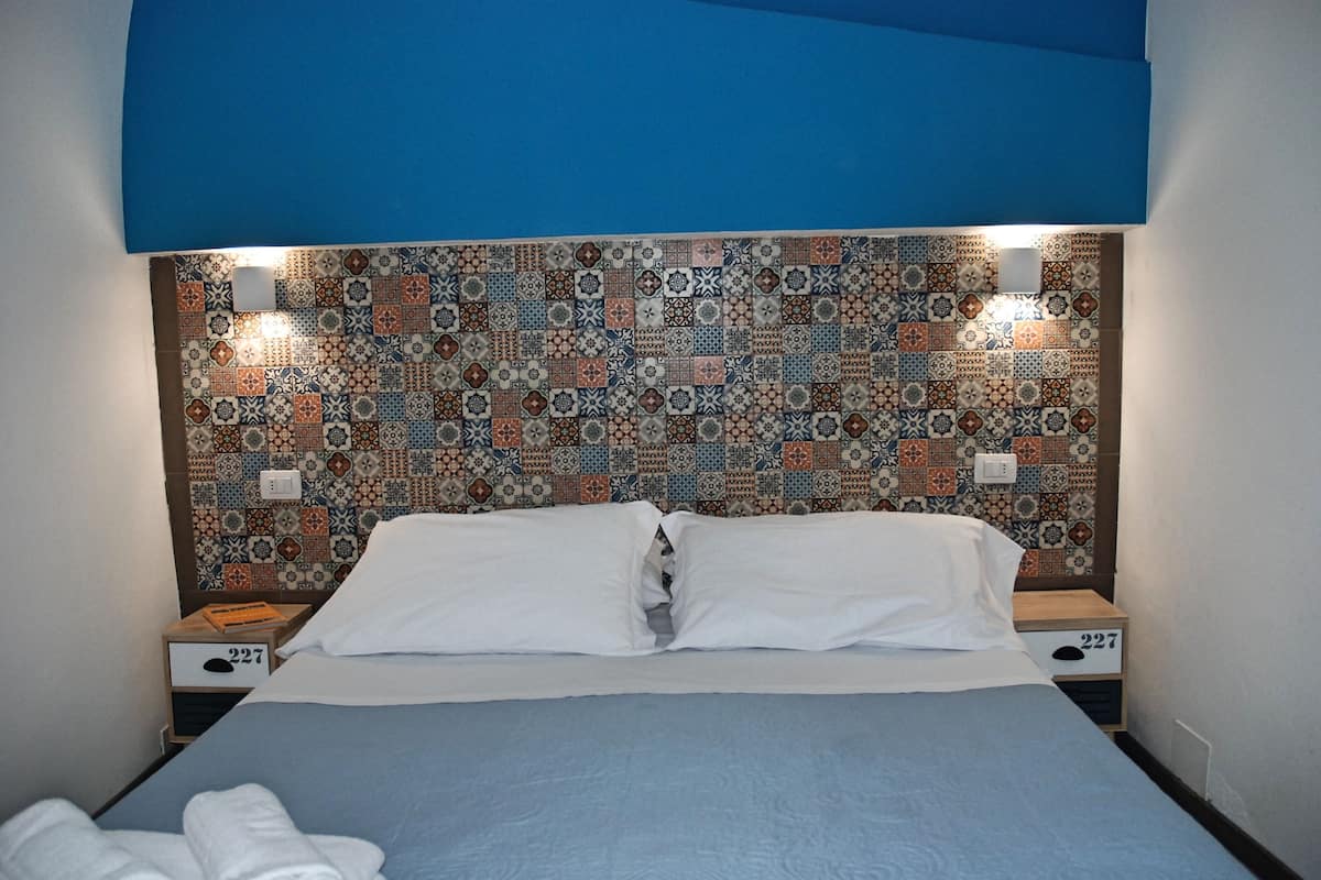 A neatly made bed with white linens, a patterned headboard, and two bedside tables with drawers.