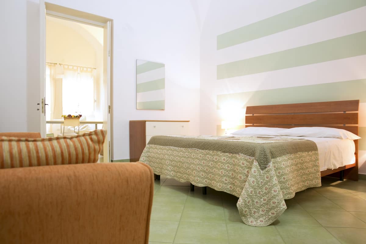 A bedroom with a bed, a chair, a bedside table, and a mirror.