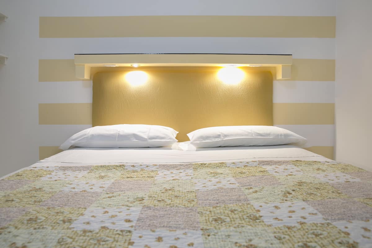 A bed with a quilt, a headboard with lights, and a wall with horizontal stripes.