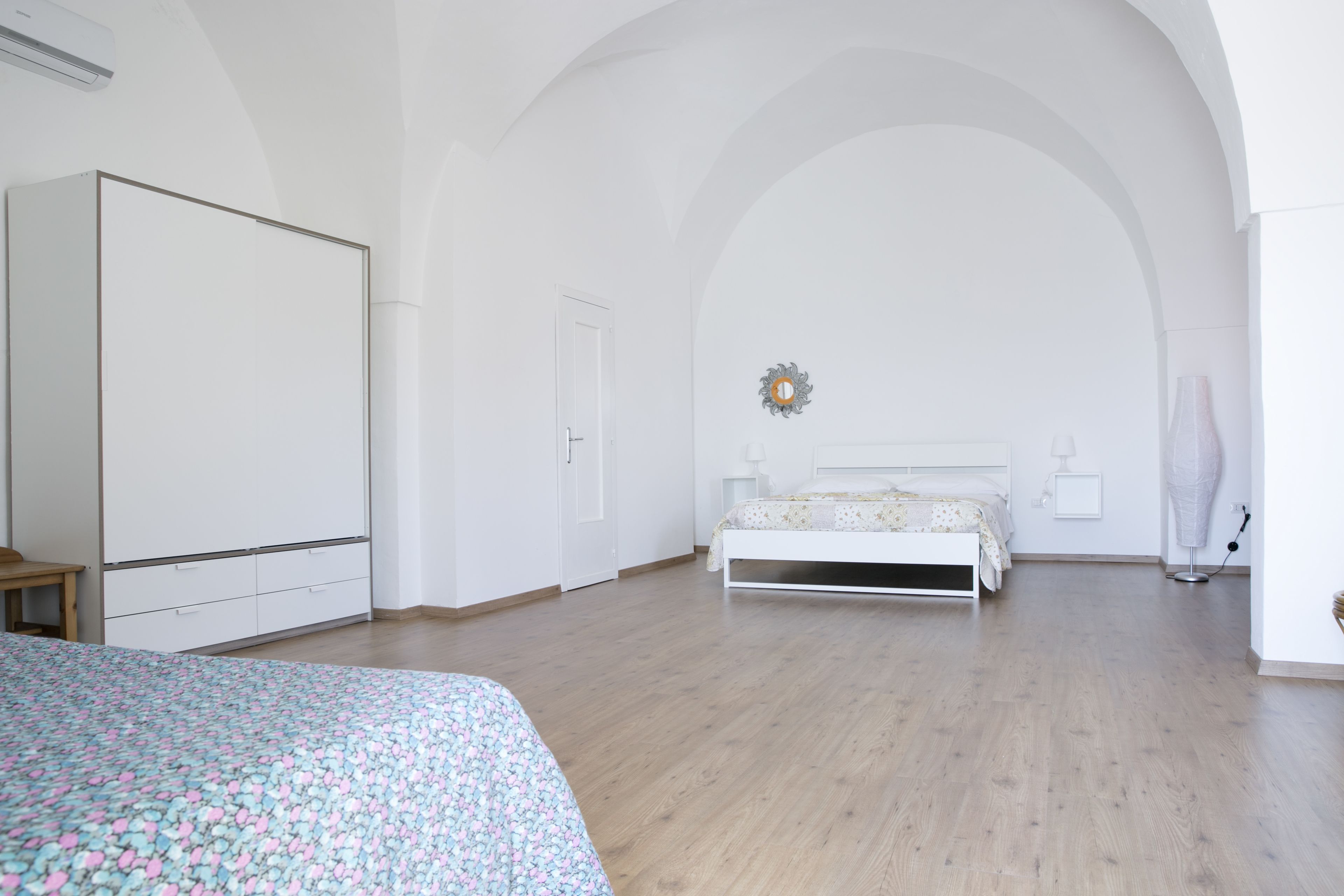 A spacious bedroom with a large bed, a wardrobe, and a door leading to another room.