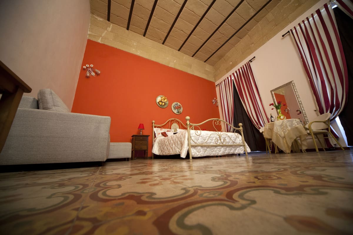A bedroom with a bed, a sofa, a table, and a mirror.