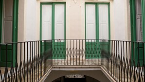 A building facade with green doors and a wrought iron balcony railing.