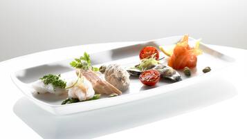 Een wit, rechthoekig bord met diverse zeevruchten, waaronder vis, garnalen en een stukje zalm, versierd met kruiden.