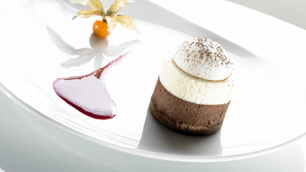 Un dessert servi dans une assiette blanche, décoré d’une feuille et accompagné de quelques fruits rouges.