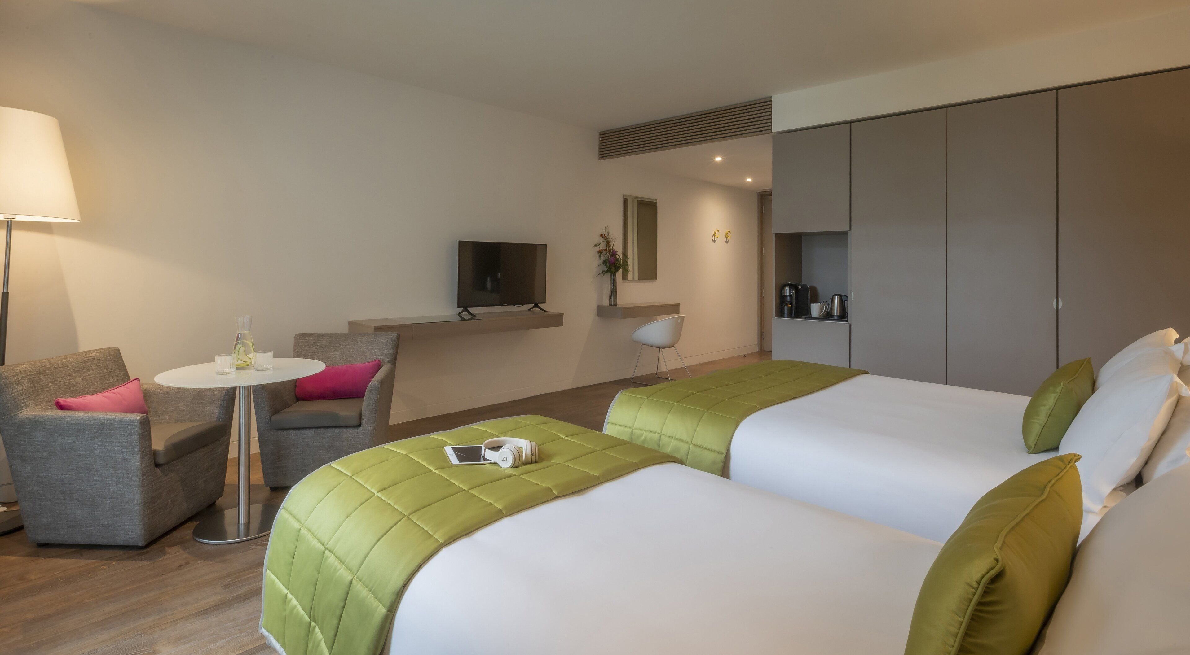 Een hotelkamer met twee bedden, een bank, een eettafeltje, een televisie en een kitchenette.