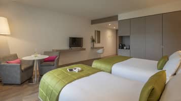 Een hotelkamer met twee bedden, een bank, een eettafeltje, een televisie en een kitchenette.