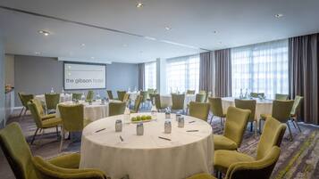 Un salón de conferencias con mesas redondas, sillas y una pantalla de proyector que muestra 'the gibson hotel'.