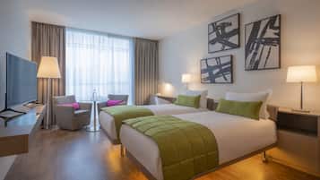 A hotel room with a large bed, two bedside tables, a desk with a chair, a TV, and a window with curtains.