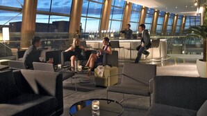 Et moderne loungeområde med siddepladser, bar og store vinduer med udsigt over bybilledet.