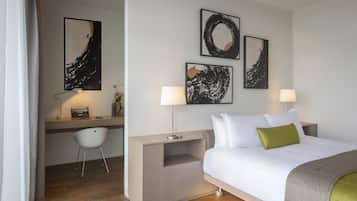 A modern hotel room with a bed, desk, and chair. There are three abstract paintings on the wall.