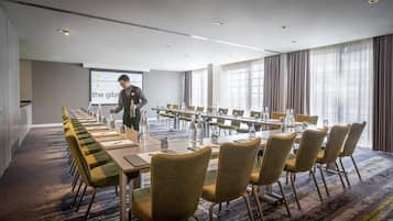 Uma sala de conferências com uma mesa comprida, cadeiras e uma tela para apresentações.