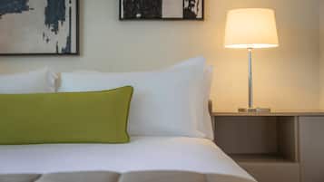 A neatly made bed with white and green pillows, a bedside lamp, and abstract art on the wall.