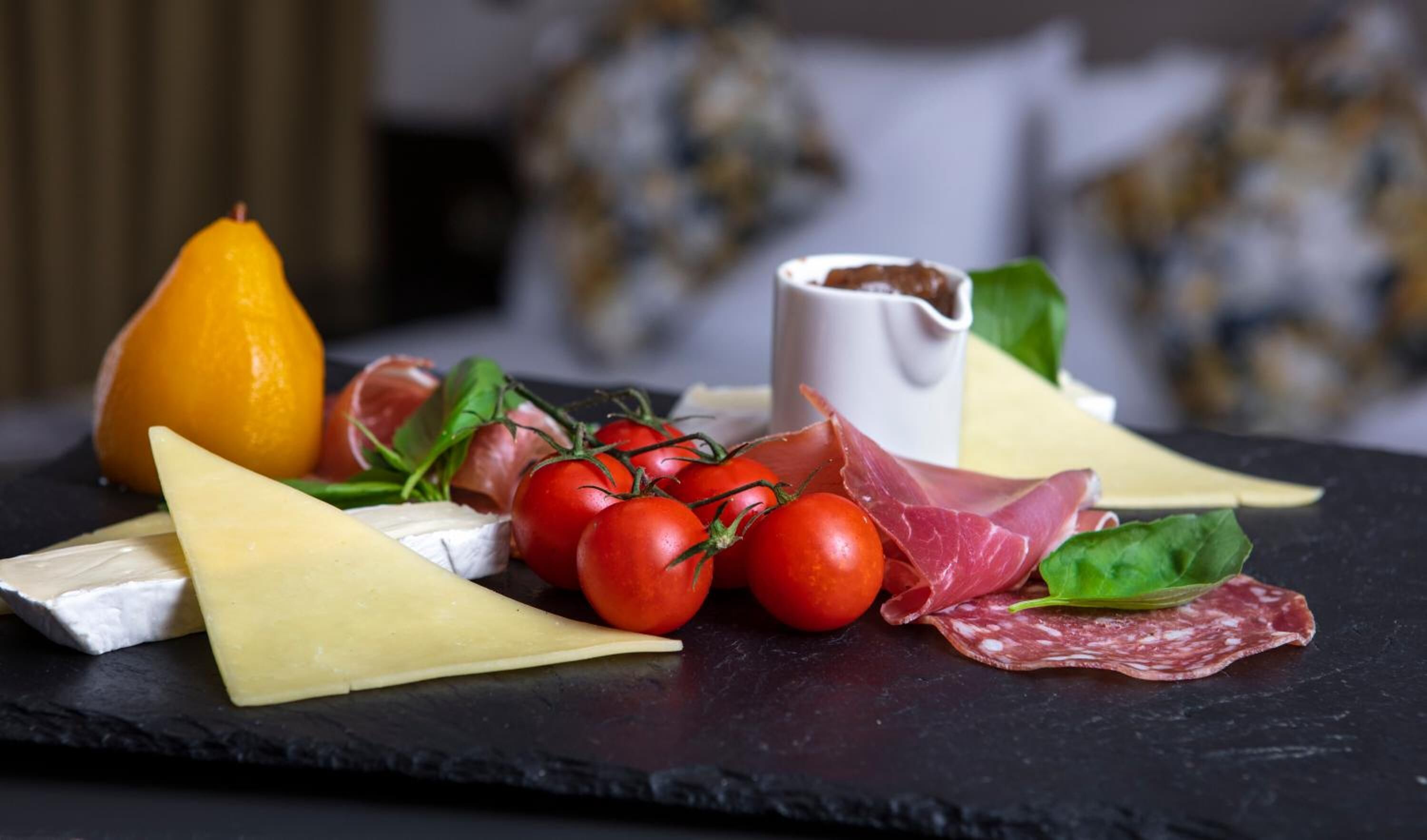 A charcuterie board with cheese, tomatoes, and cured meats on a slate board.
