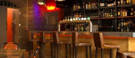 Zona de bar con taburetes de madera, mostrador y estantes llenos de botellas.