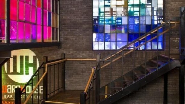 Een trap leidt naar een bar met een groot raam dat kleurrijke verlichting toont.