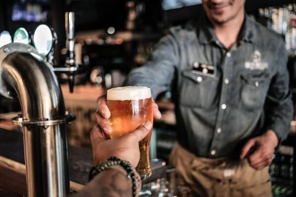 A person holding a glass of beer at a bar with a tap and a bartender in the background. - McGettigan's Hotel Letterkenny (Letterkenny)
