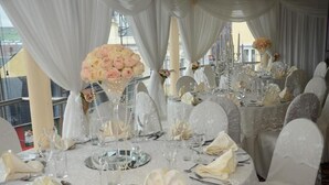 Een feestzaal met ronde tafels, gedekt voor een formeel evenement, met witte tafelkleden, glazen en bloemstukken als decoratie.