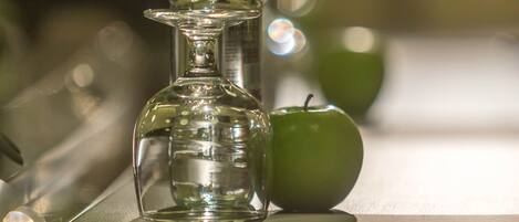 A clear glass bottle with a narrow neck and a wider base, positioned on a reflective surface with a green apple nearby.