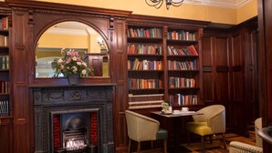 A library with a fireplace, bookshelves, and two chairs. - Cahir House Hotel (Cahir)