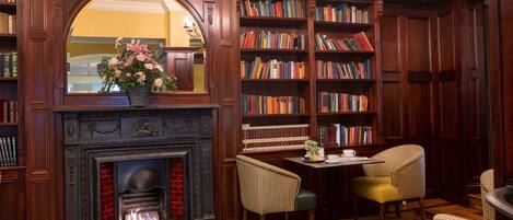A library with a fireplace, bookshelves, and two chairs.