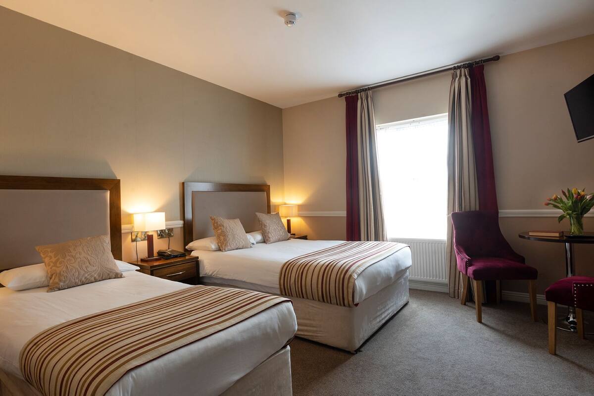 A hotel room with two beds, a desk, a chair, and a window with curtains.