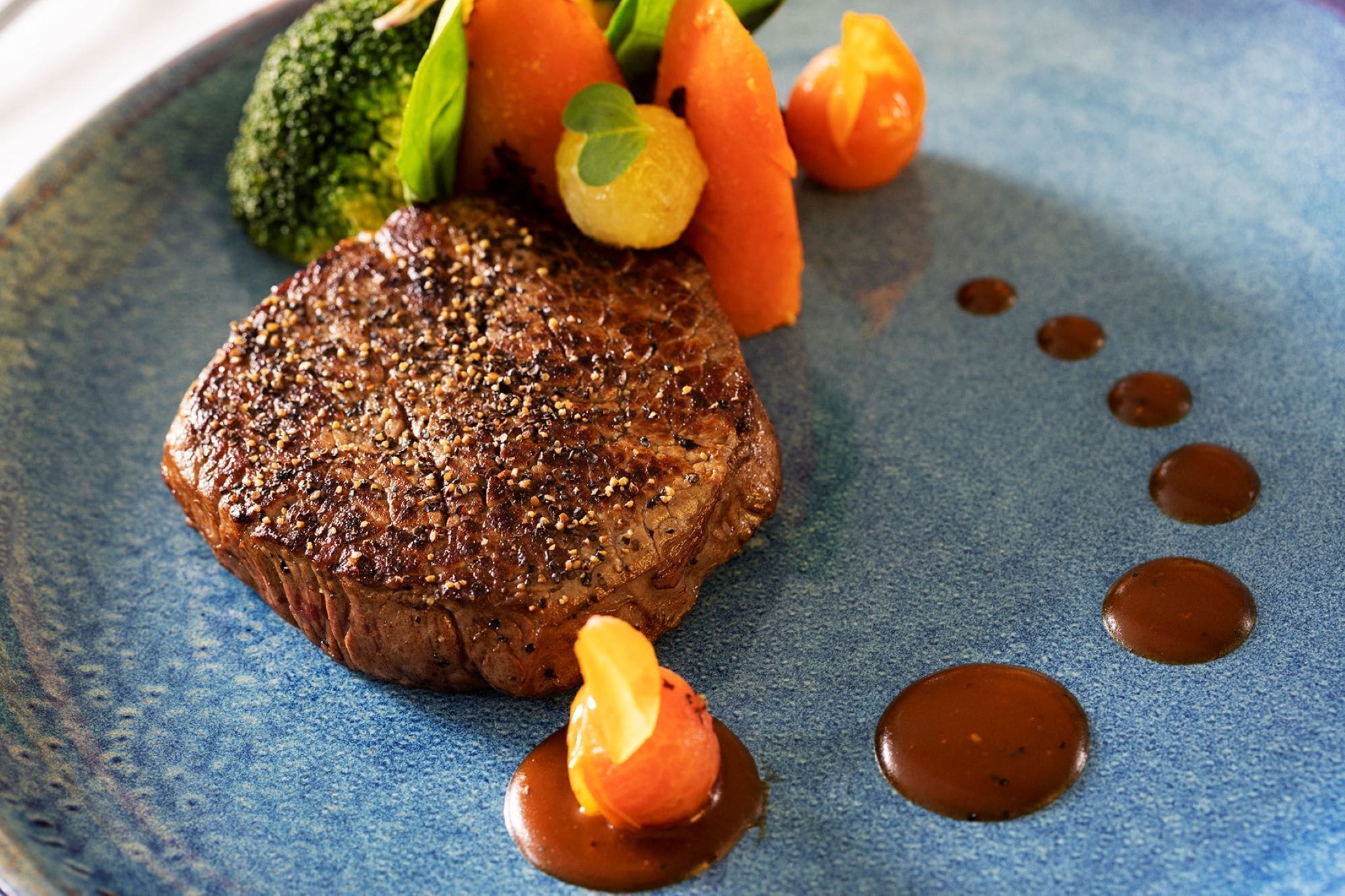 Un steak accompagné de légumes et de sauce, servi dans une assiette bleue.