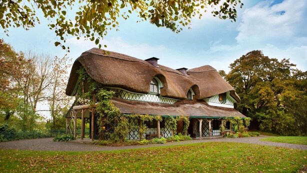 A large, rustic house with a thatched roof and ivy-covered walls, surrounded by a well-maintained garden and trees. - Cahir House Hotel (Cahir)