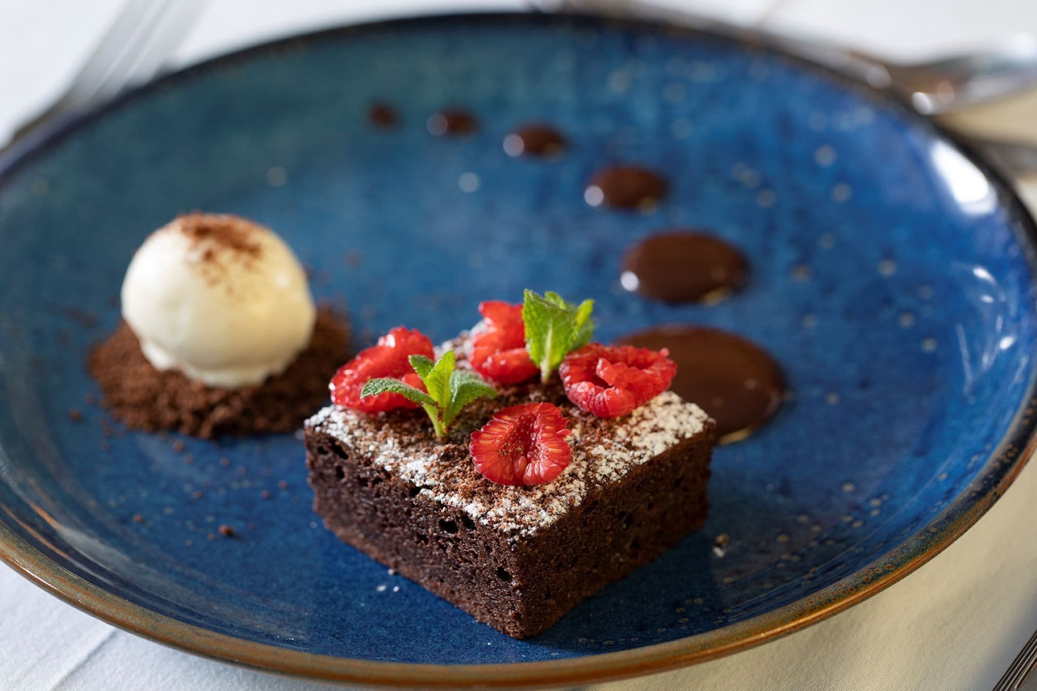 A dessert on a blue plate with a scoop of ice cream and strawberries on top.