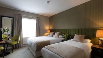 Une chambre d’hôtel avec deux lits, un bureau avec une chaise, un miroir et une fenêtre avec des rideaux.